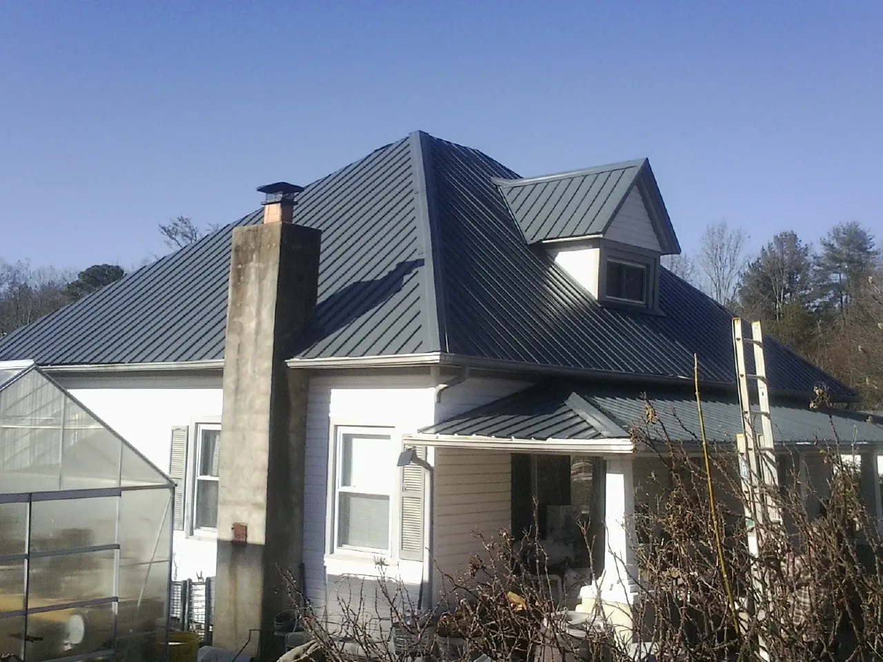Dark blue standing seam metal roof on a white farmhouse with dormer — Slate & Tile Roof Repair by Roofing Brothers in Reasnor