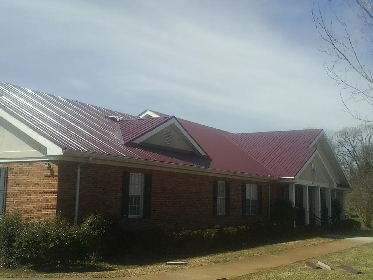 Red metal roof with gabled entries on a long brick building, from a Hail Damage Roof Repair job in Reasnor