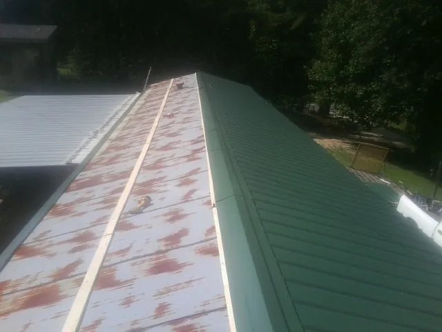 Old rusted panels beside newly installed green metal roofing — Wind Damage Roof Repair by Roofing Brothers in Reasnor