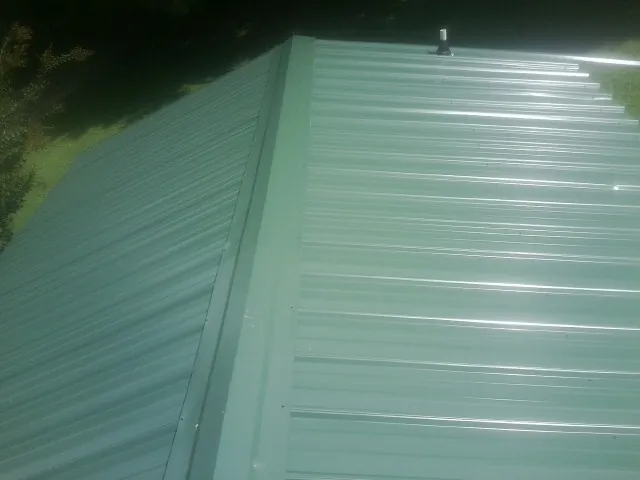 New green metal panels meeting at the ridge of a roof — Flat Roof Repair work by our crew in Reasnor