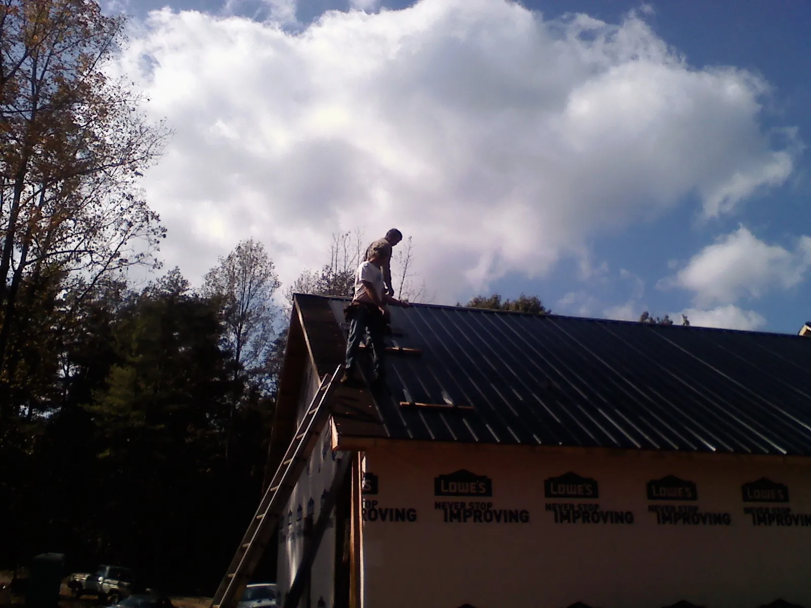 Roofer fastening dark metal panels high against a cloudy sky, from a Roof Inspection job in Reasnor