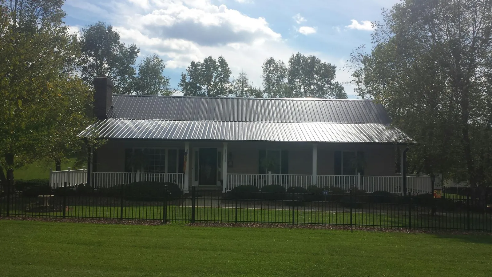 Gray metal roof on a brick ranch with a full width front porch — Gutter Guard Installation work by our crew in Reasnor