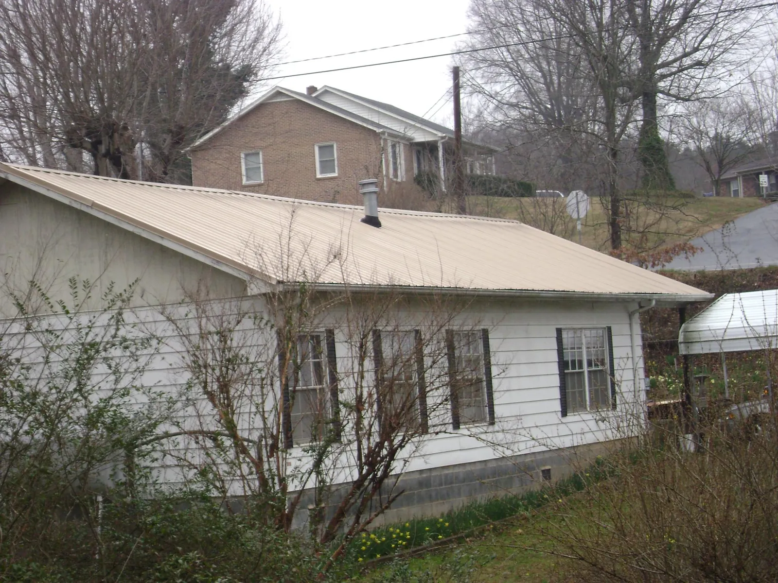 Tan metal roof on a white sided house set into a hillside — Commercial Roofing by Roofing Brothers in Reasnor