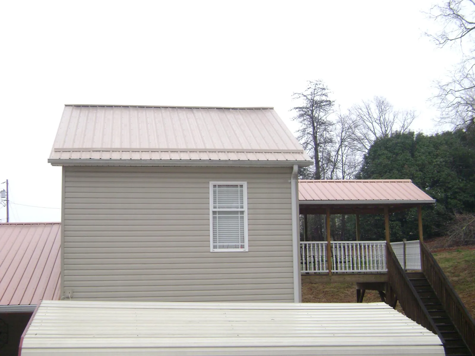 Tan metal roofs on a two story addition and attached porch, from a Roof Replacement job in Reasnor